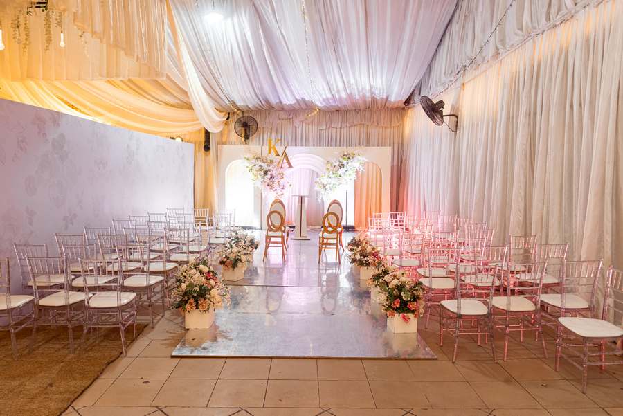 The marquee set for a ceremony, chiavari chairs either side of a clear aisle, florals and a draped canopy.